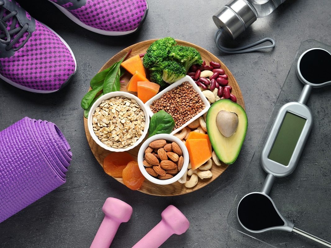 Plate with heart-healthy products and sports equipment on grey b